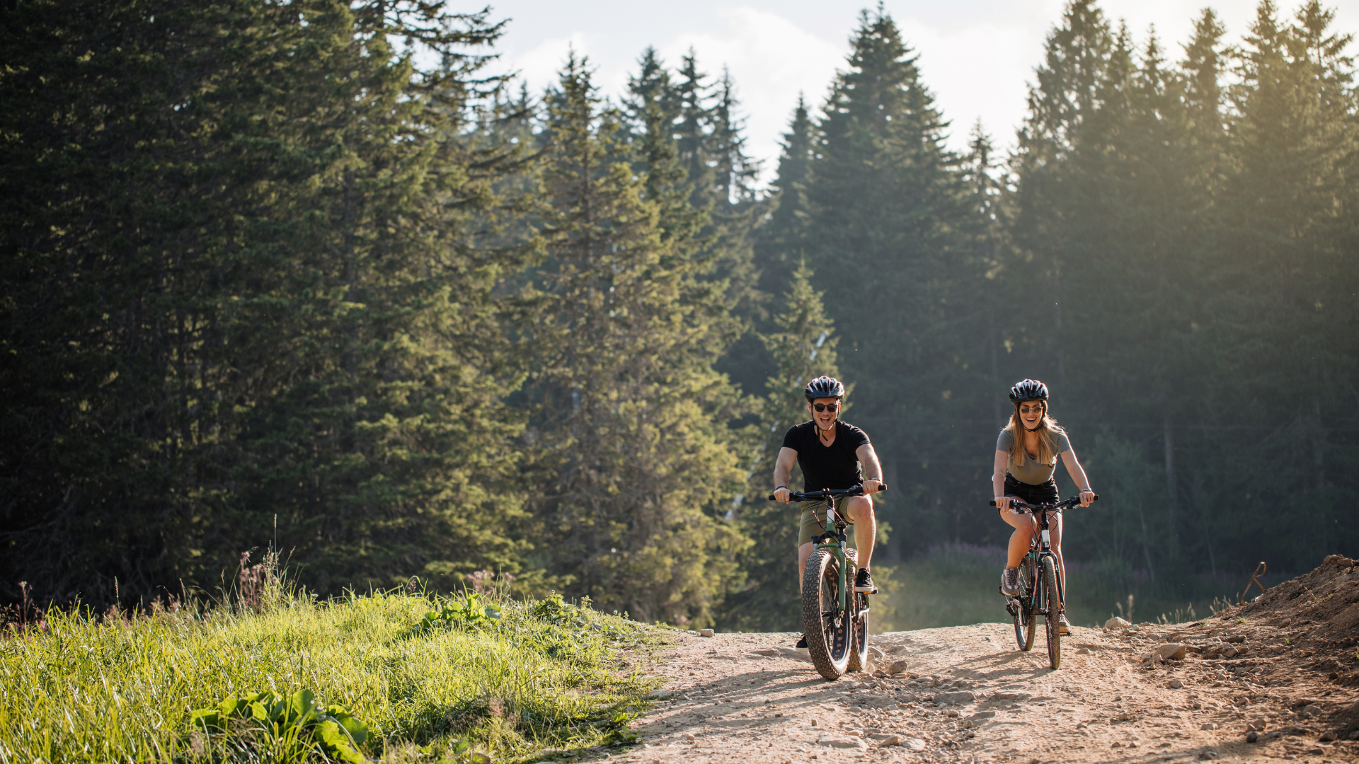 Couple souriant à vélo électrique sur un chemin de terre, lumière du soir en Provence