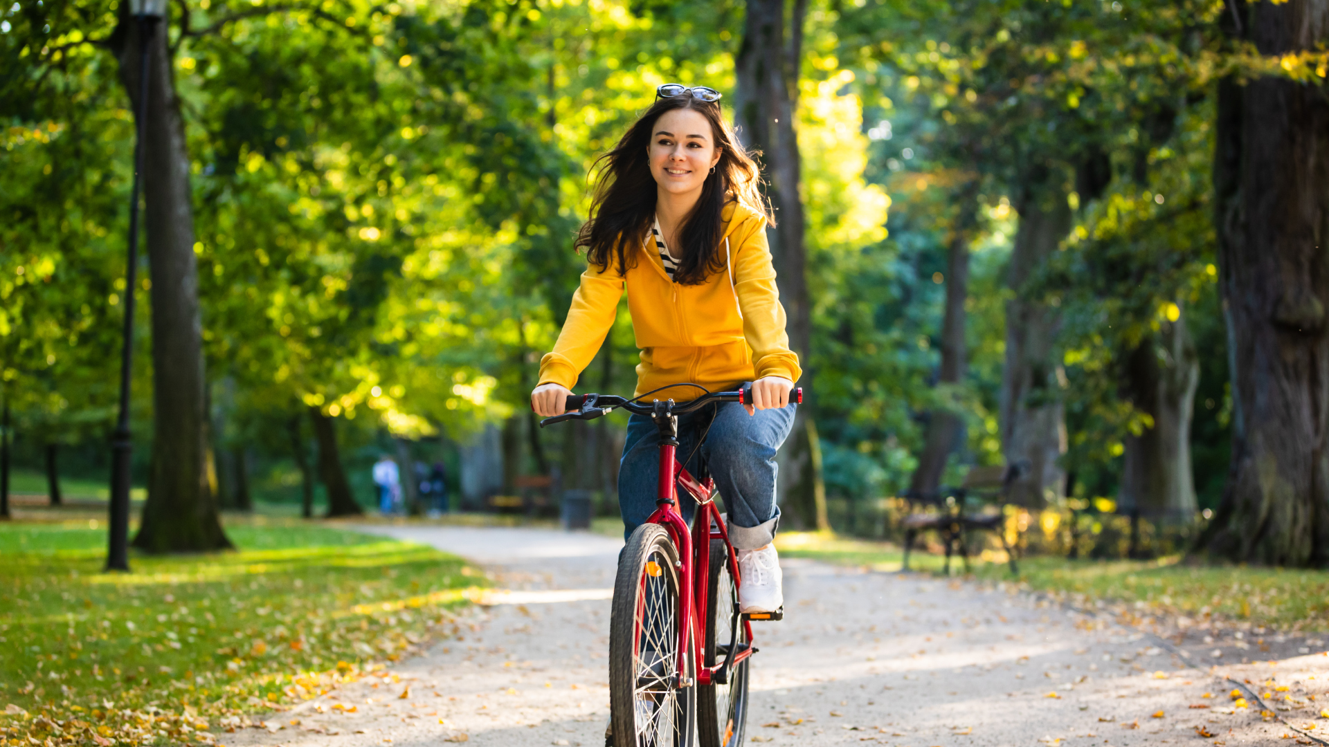 Jeune femme souriante à vélo électrique rouge dans une allée ensoleillée en Provence