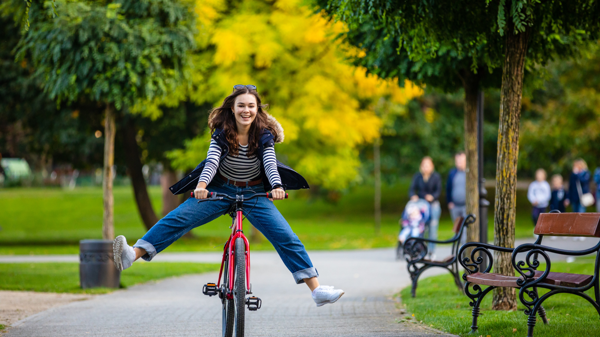 Jeune femme souriante à vélo électrique rouge dans un parc en Provence, lumière automnale