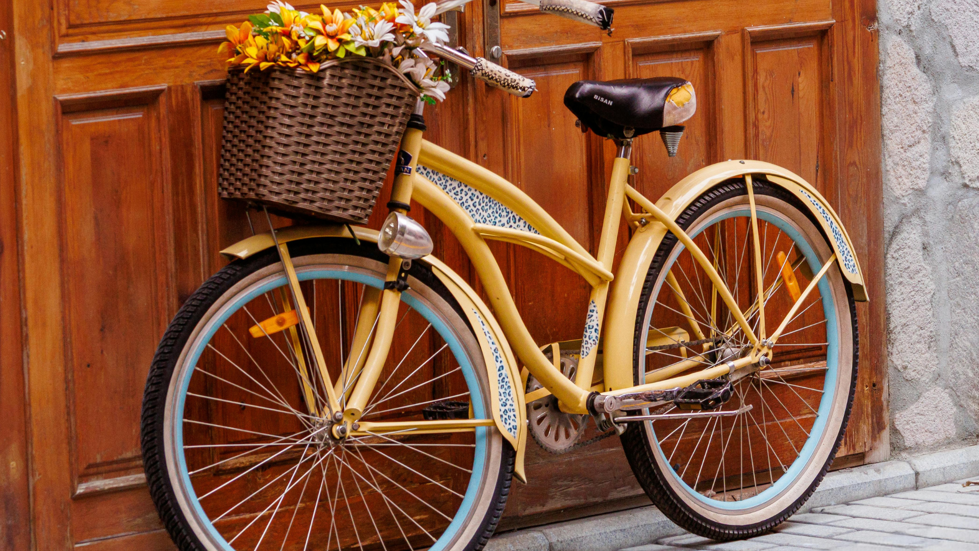 Vélo cruiser jaune pastel avec panier en osier fleuri devant une porte en bois ancienne, dans un village de Provence