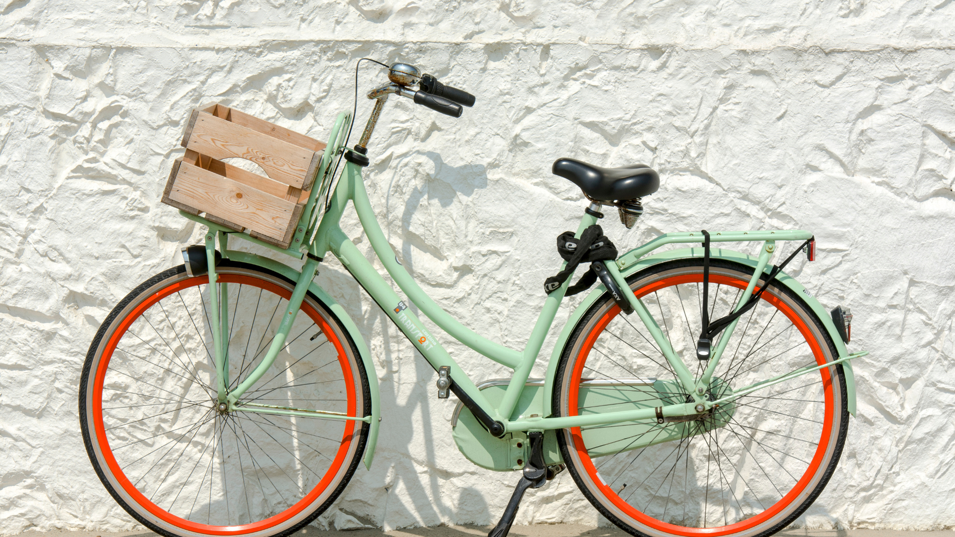 Vélo hollandais vert menthe avec cagette en bois et jantes orange, contre un mur blanchi à la chaux dans un village de Provence
