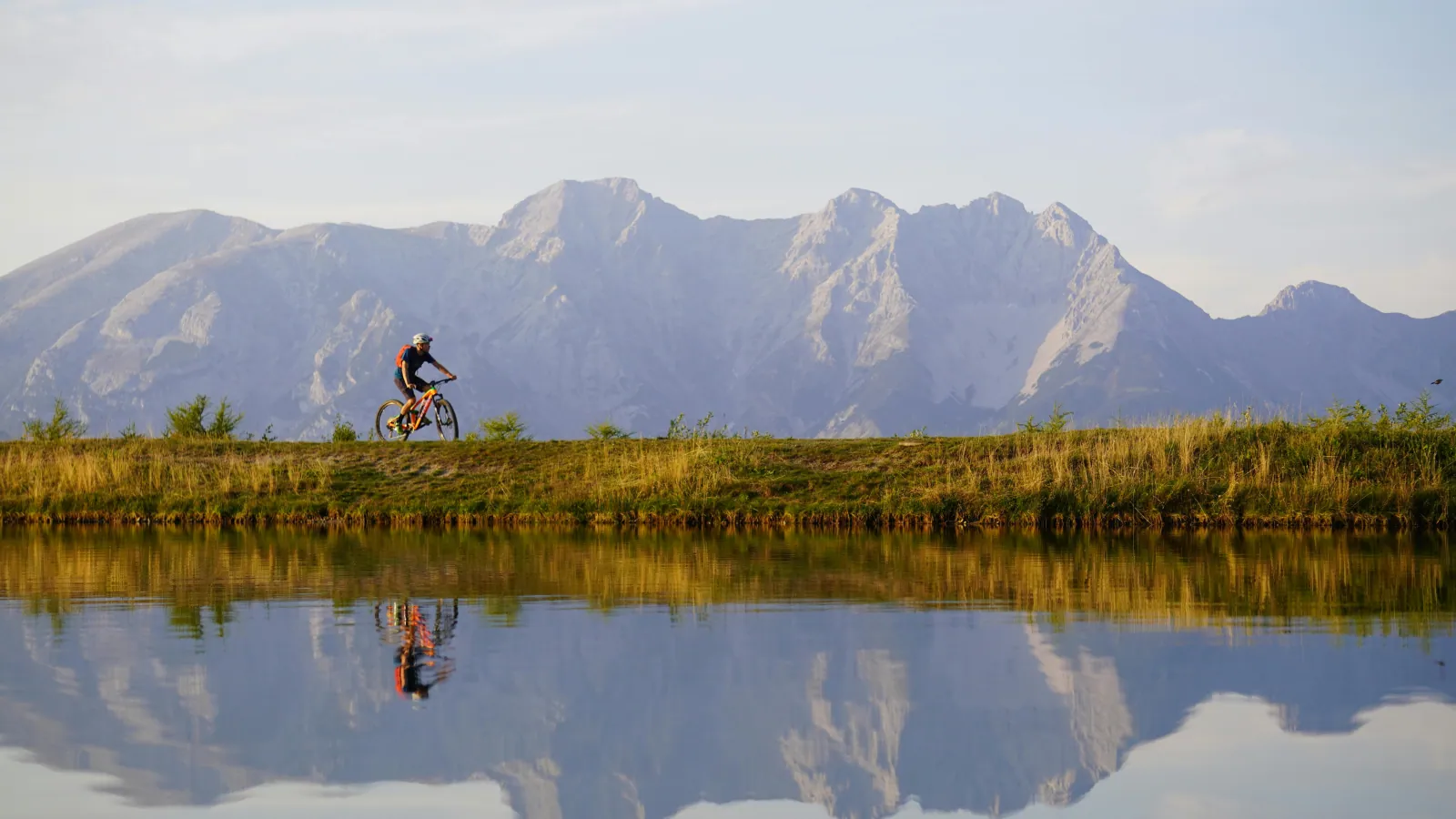 Cycliste le long d'un plan d'eau, avec les montagnes en reflet